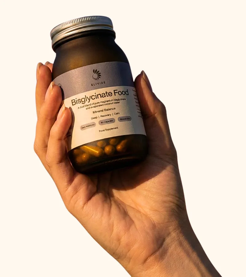 Hand holding amber glass bottle of Bisglycinate Food supplement with silver lid against light background