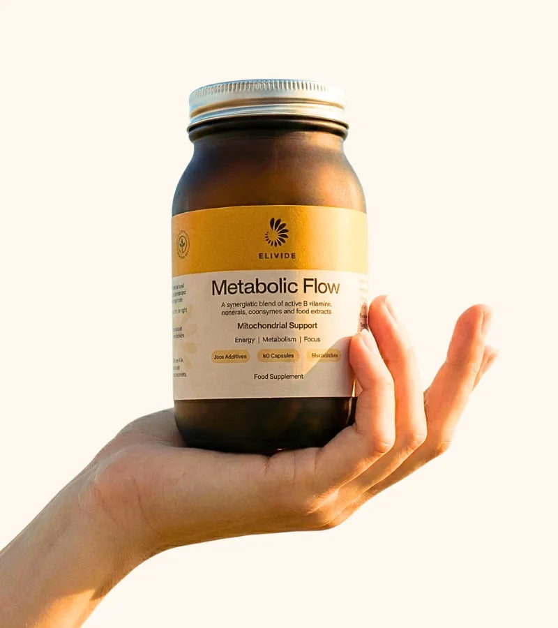 Hand holding Metabolic Flow supplement jar with amber glass and gold label showing mitochondrial support formula