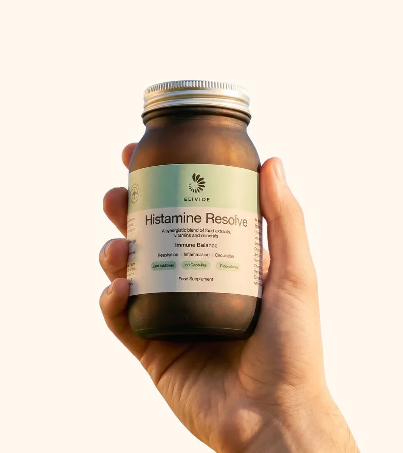 Hand holding amber glass jar of Histamine Resolve supplement with silver lid against cream background